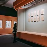 woman in black jacket standing in front of white framed photos