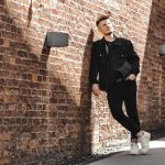 man in black leather jacket and black pants leaning on brown brick wall