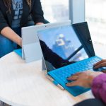 two person using laptop computers beside glass window
