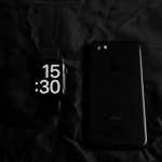 a black cell phone sitting next to a black clock