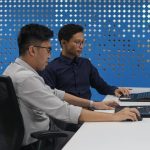 two men sitting at a table with laptops