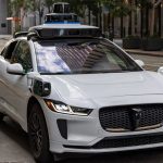 A white self-driving car on a city street.