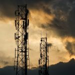 A couple of cell towers sitting under a cloudy sky