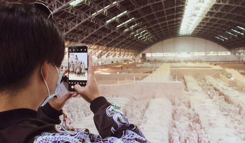 woman in black and white floral dress taking photo of a train station
