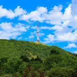 A tall tower stands on a green, tree-covered hill