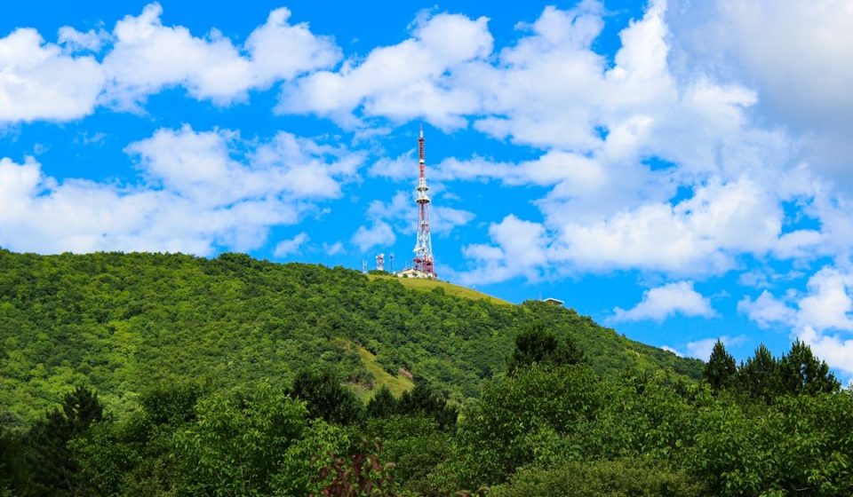 A tall tower stands on a green, tree-covered hill