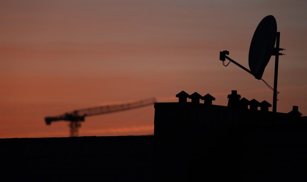 Satellite dish and crane silhouetted against sunset sky