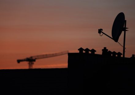 Satellite dish and crane silhouetted against sunset sky