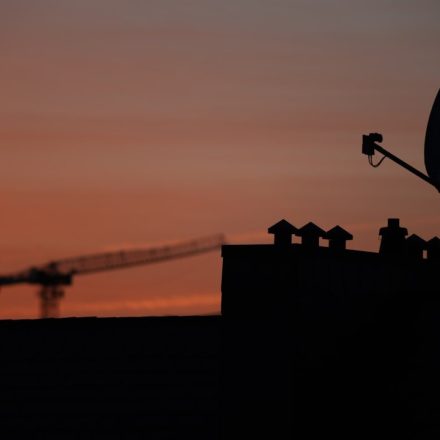 Satellite dish and crane silhouetted against sunset sky