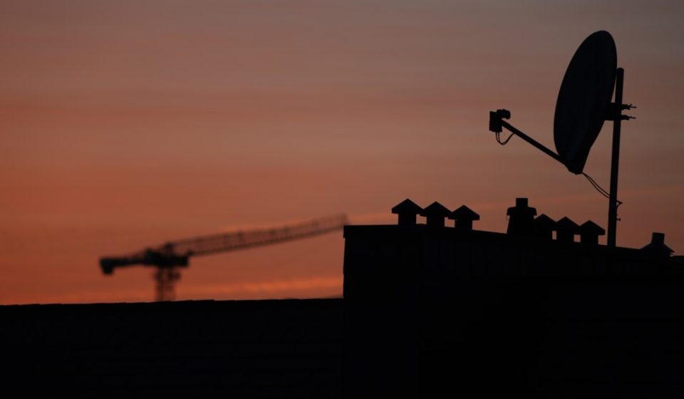 Satellite dish and crane silhouetted against sunset sky